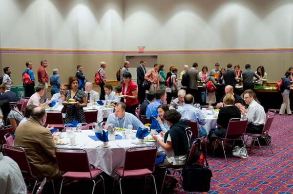 Groups of people sit around three round tables as part of a conference at the Oregon Convention Center.