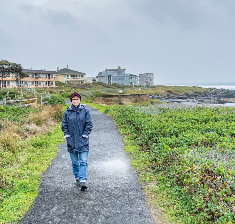 A woman walks down a beachside path on a gloomy day.